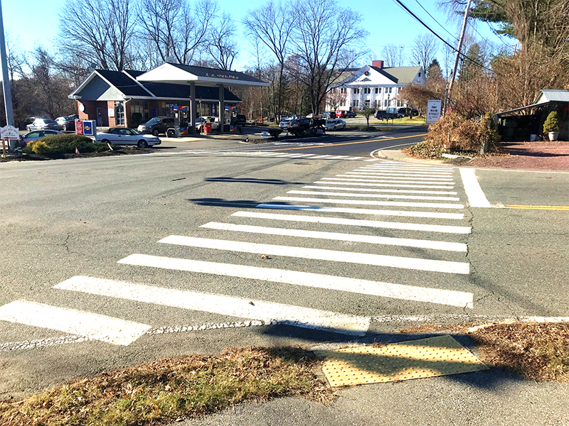 Figure 7 - View across Library Hill Road of Northwest Intersection Corner. Image shows a crosswalk leading to the former One Main Street Studio florist in the foreground and the Stow Building Department on the south side of Great Road (Route 117) in the background.